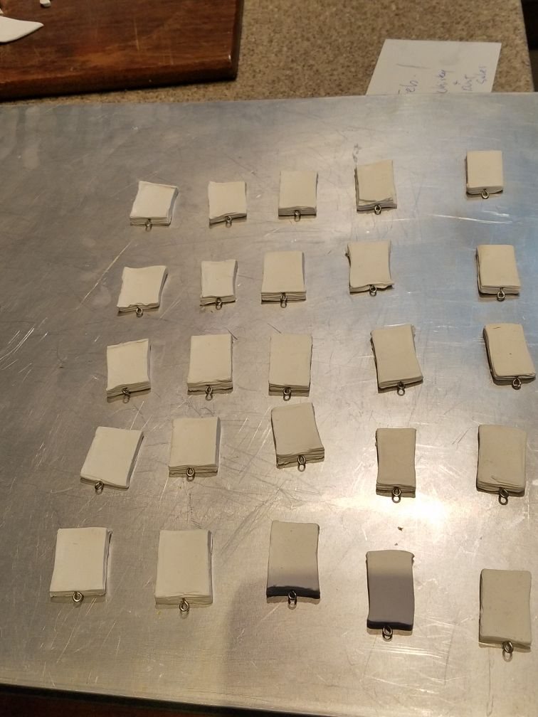 Two dozen baked clay book blanks with screw eyes on a metal baking sheet