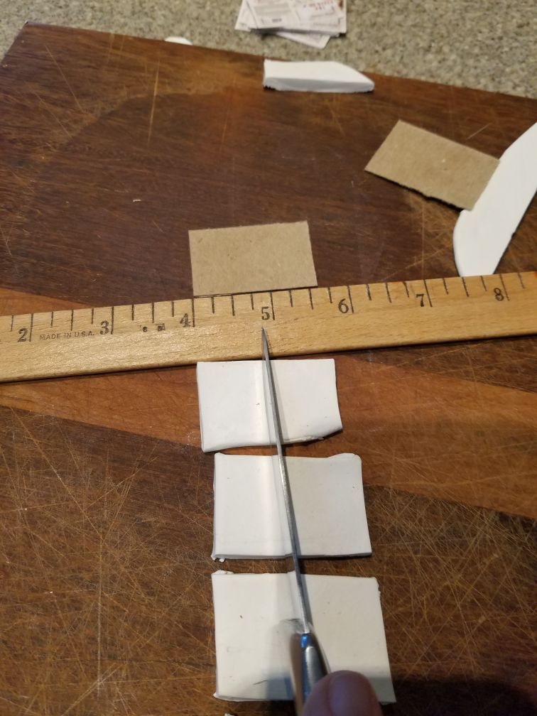 A knife cutting rolled white clay into rectangles along a wooden ruler