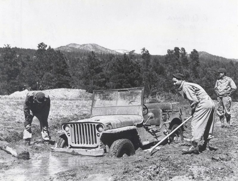 Historic photograph of men digging out a jeep stuck in mud at Los Alamos